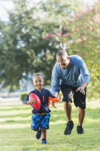 Dad and toddler son playing football in the park