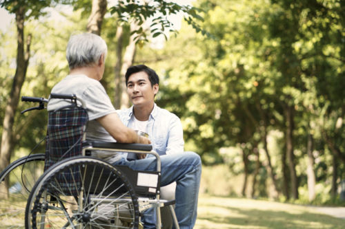 Asian father in wheelchair talking with son.