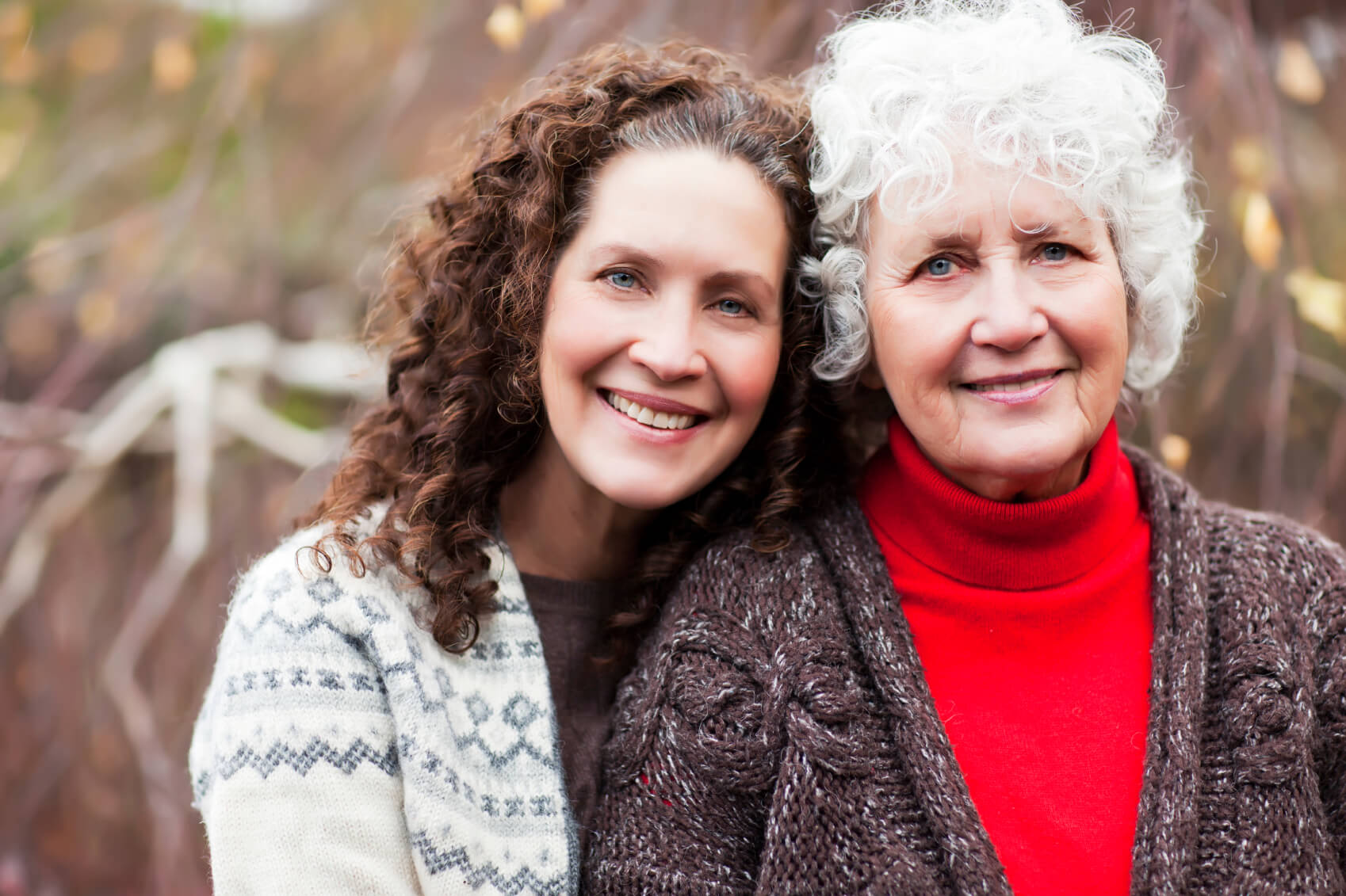 Middle aged women with brown curly hair smiling with her older mother, who has grey curly hair.