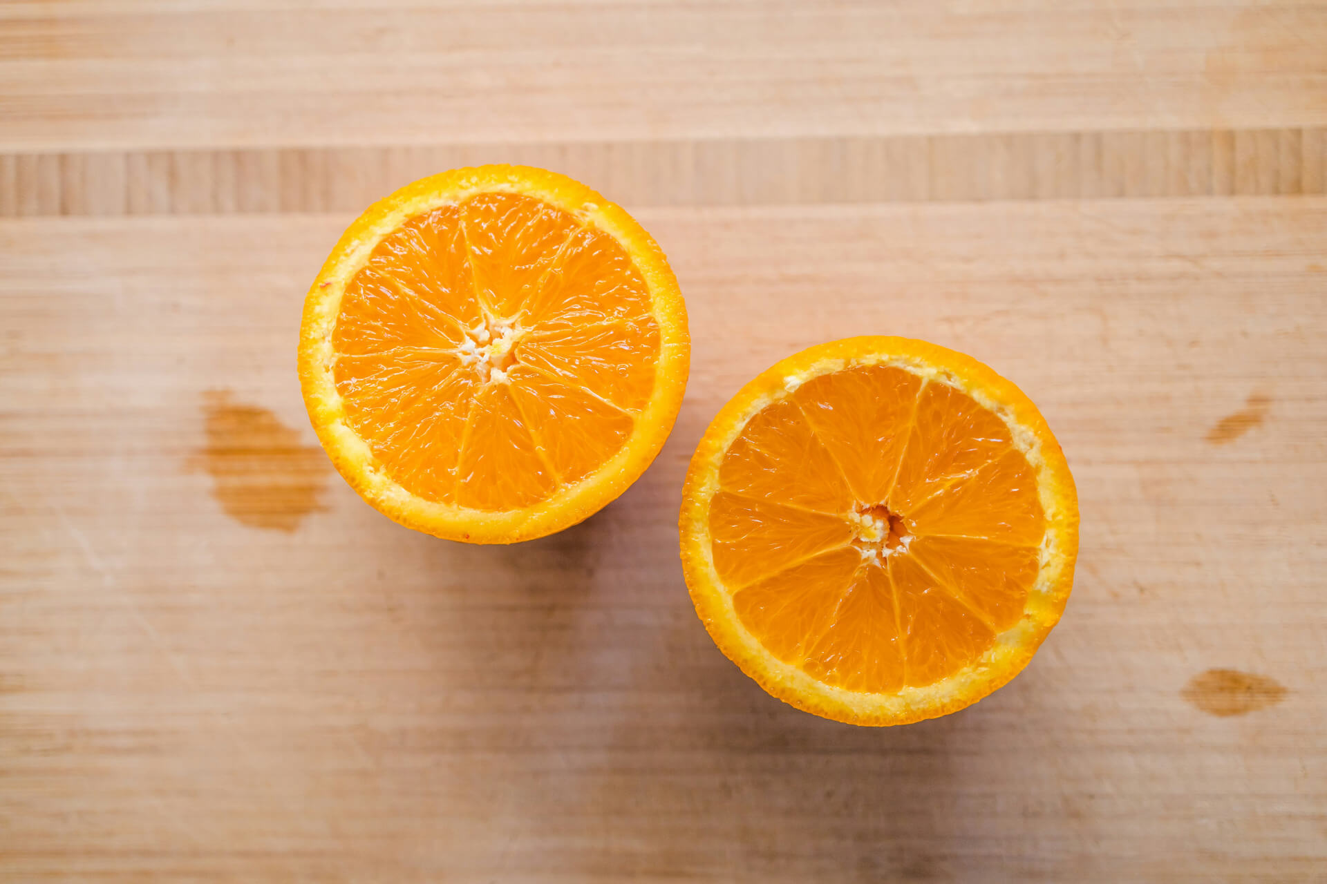 A naval orange sliced in half laying on a wood cutting board.