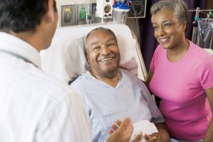 Older black man in hospital bed. Older black woman and white doctor standing at the bedside